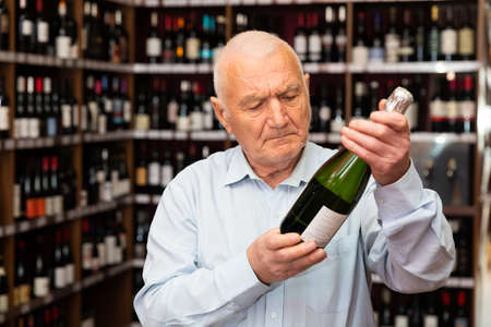 Attentive elderly man chooses champagne in a liquor storeの写真素材