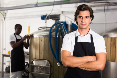 Young man brewer in uniform is standing in brew-houseの写真素材