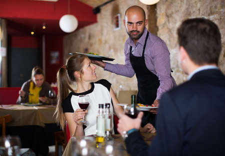 waiter bringing ordered dishes to smiling coupleの写真素材