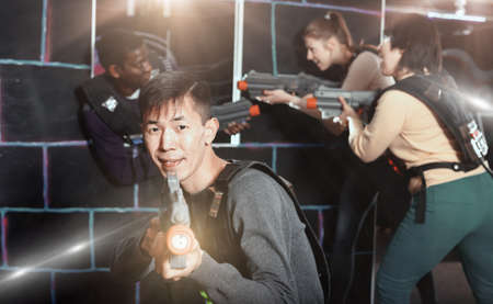 Emotional Asian man with laser pistol playing laser tag with friの写真素材