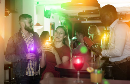 Male bartender shaking cocktail mixer for couple at nightclub