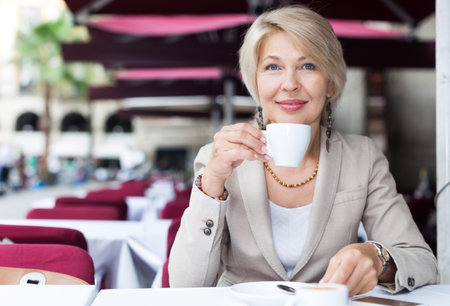 Portrait of elegant mature female who is enjoying of lunch with coffee