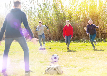 Cheerful teenagers are jogning with ball in park