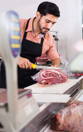 Adult male butcher is cutting meatの写真素材