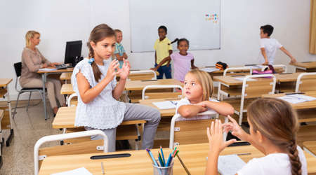 Positive primary school students are talking about homework at deskの写真素材