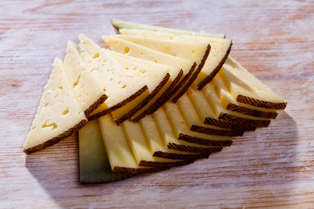 Slice of semi-hard cheese on a wooden tableの写真素材