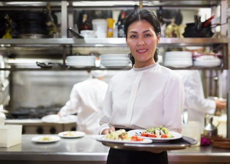 portrait of smiling female waiter standing in kitchen in restaurante