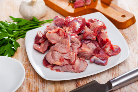 Raw chicken gizzards and greens on wooden surface