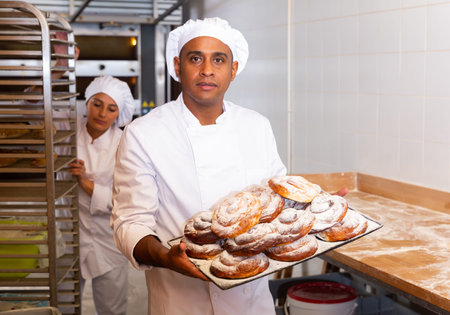 Smiling bakery worker carrying tray with baked ensaimadas