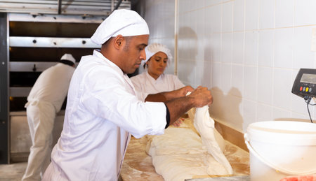 Professional baker working with raw yeasted dough in bakery