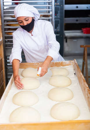Professional baker wearing protective mask prepares raw loaves for baking in ovenの写真素材