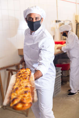 Baker taking baked bread out of oven on wooden shovelの写真素材