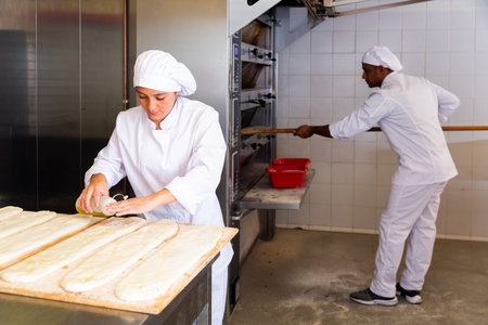Woman baker pouring oil on raw cocas before baking