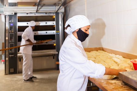 Woman baker dividing raw dough into portions in bakery