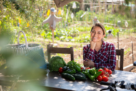 Young woman sits at table with ripe vegetables in the backyard of village house