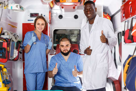 Portrait of three happy paramedicals posing in ambulance carの写真素材