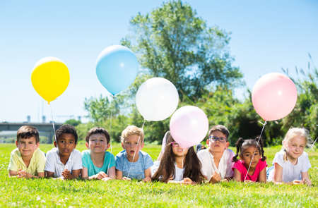 Happy kids with balloons lie on the green lawnの写真素材