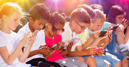 Children using mobile devices outdoors at sunny dayの写真素材