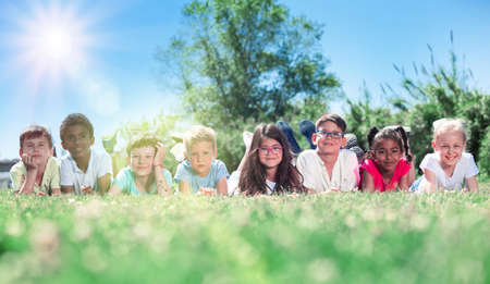 Happy children lie on the green grass on a sunny dayの写真素材