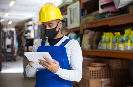 Worker in protective mask taking inventory in building materials store