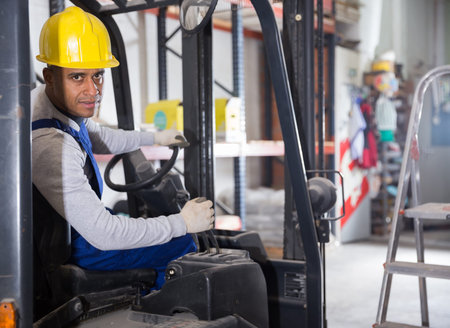 Hispanic worker of building materials warehouse driving forklift truck