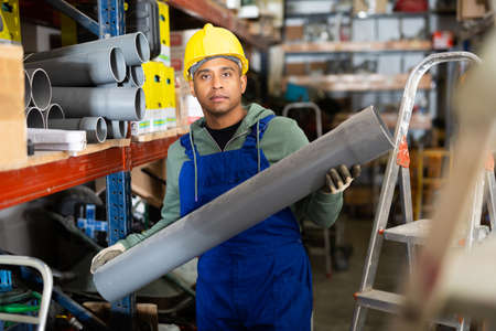 Plumber in protective helmet and overalls selects plastic pipes in hardware storeの写真素材