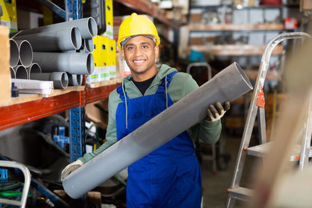 Plumber in protective helmet and overalls selects plastic pipes in hardware store