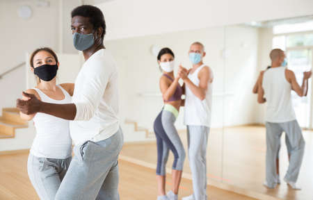 Couple in masks learning to dance waltz during group trainingの写真素材