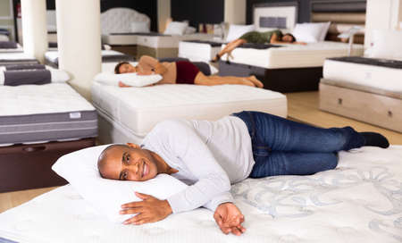 Smiling hispanic man lying on orthopedic mattress in furniture storeの写真素材