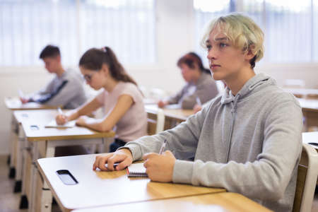 Smart teenager listening to lecturer and writing in notebookの写真素材
