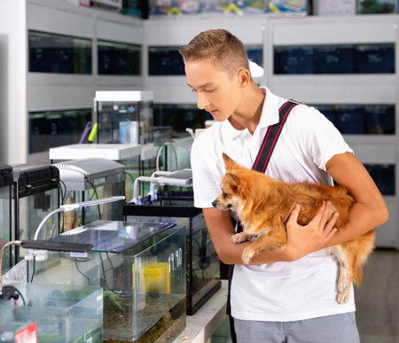 Young man with dog standing near aquarium in pet shop