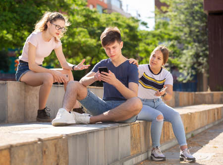 Teenage boy absorbed in phone, ignoring girls talking to himの写真素材