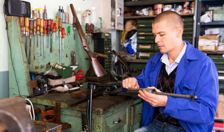 Male gunsmith repairing hunting rifle in workshopの写真素材