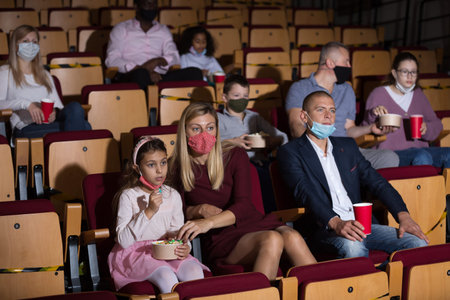 People in protective masks absorbedly watching movie in cinema