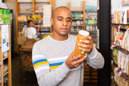 Focused man reading product contents on jar in grocery store