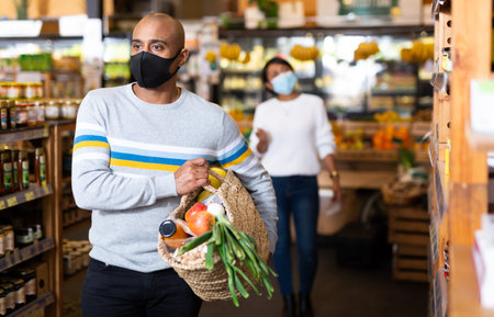 Shopper wearing protective mask with bag of groceries and vegetables at grocery supermarketの写真素材