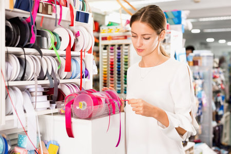 Interested young woman choosing colorful ribbons and braid for dressmaking in sewing supplies shopの写真素材