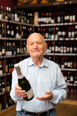 Attentive elderly man chooses champagne in a liquor storeの写真素材