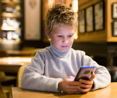 Tween boy carried away with phone at table in cafeの写真素材