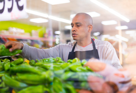 Spanish employee in vegetable store with green peppersの写真素材