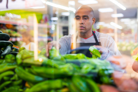 Merchandiser in an apron lays out ripe bell peppers on supermarket counterの写真素材