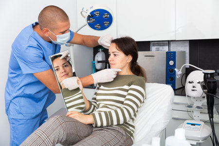 Cosmetologist examining female client face before procedureの写真素材
