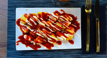 Top view of Patatas bravas, Spanish dish of fried potatoes served with cheese sauce and spicy sauce...