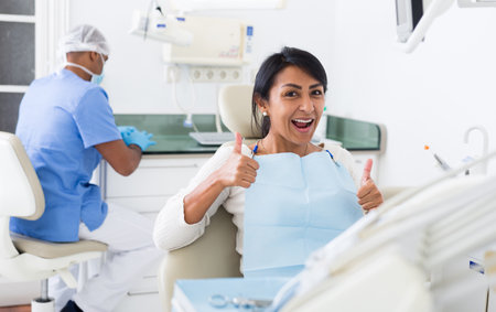 Happy woman sitting in dental chair after teeth cure in clinicの写真素材