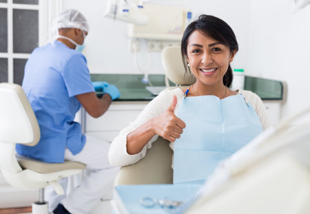 Satisfied Latina in dental office showing thumbs up after treatmentの写真素材
