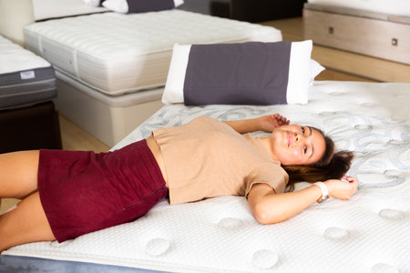Smiling happy woman testing new mattress in furniture storeの写真素材