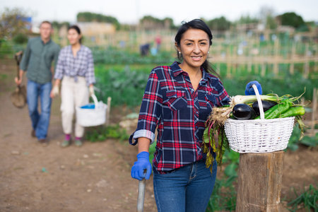 Happy hispanic woman showing vegetable crop in kitchen gardenの写真素材