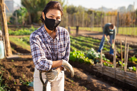 Portrait of female farmer in protective mask with shovel on farm fieldの写真素材