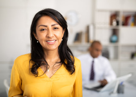 Smiling hispanic woman employee posing in office interiorの写真素材