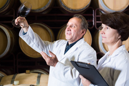 Worker of winery holds glass of red wine in hand and shows him to expert